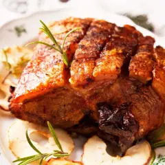 Ein knuspriger Krustenbraten aus dem Backofen, garniert mit Rosmarin und Apfelringen auf einem festlichen Teller.