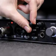 Dłoń kręci pokrętłem "MIX" na interfejsie audio, przygotowując się do podłączenia telefonu do wzmacniacza.