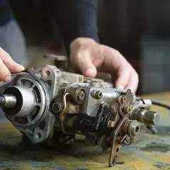 Man's hands work on a diesel injection pump. A mechanic's careful touch shows that it deserves to be fixed.