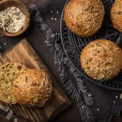 Świeże bułeczki z ziarnami na desce i w koszyku. Idealne po rozmrożeniu w piekarniku.