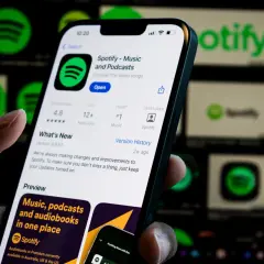 Dłoń trzyma smartfon z otwartą aplikacją Spotify. W tle widać ikony Spotify.