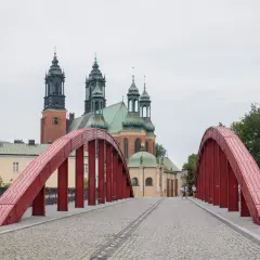 Czerwony most na poznańskiej trasie prowadzi do katedry. Spacerowicze podziwiają architekturę.