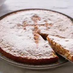 Tarta de Santiago, espolvoreada con azúcar glas, con una porción servida.