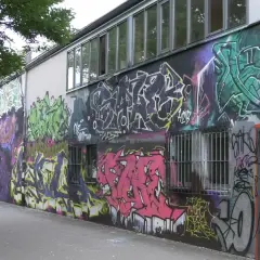 Bunte Graffiti-Kunst bedeckt die Wand eines Gebäudes, mit Fenstern und einer Tür.