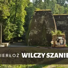Grupa turystów zwiedza historyczny Wilczy Szaniec w Gierłoży, podziwiając potężne bunkry w otoczeniu zieleni.
