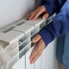 Manos frías tocan un radiador de calefacción central que no calienta.