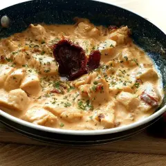 Kawałki kurczaka w kremowym sosie z suszonymi pomidorami i natką pietruszki. Danie "marry me chicken" wygląda apetycznie.