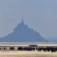 Silhouetten von Menschen auf dem Wattboden, die sich dem majestätischen Mont Saint-Michel nähern.