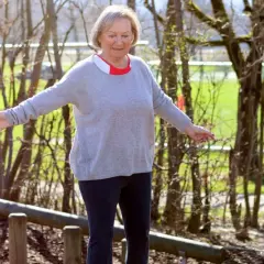 Ältere Frau balanciert auf Holzstämmen im Freien.