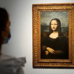 Eine Person mit Maske betrachtet die Mona Lisa. Ihre rätselhafte Bedeutung fasziniert seit Jahrhunderten.