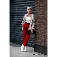 Elegancka kobieta w czerwonych spodniach i wzorzystej marynarce, z czarną torebką na łańcuszku. Stylowe czerwone spodnie stylizacje.