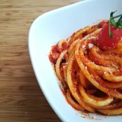 Pyszne spaghetti z sosem pomidorowym i startym parmezanem, ozdobione pomidorkiem. Idealne do przygotowania według przepisu na guanciale.