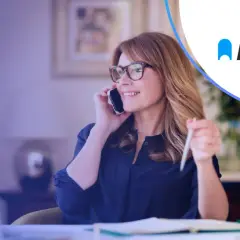 Kobieta w okularach rozmawia przez telefon, pracując przy laptopie. Rozwiązania autopay mobility ułatwiają jej codzienne życie.