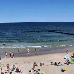Słoneczna plaża w Dźwirzynie, ludzie kąpią się w morzu i odpoczywają na piasku. To jedne z wielu atrakcji tego miejsca.