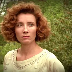 Emma Thompson w filmie, z burzą rudych loków i w jasnej sukni, spogląda zamyślona na tle zieleni.