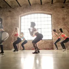 Grupa kobiet ćwiczy zumbę dla początkujących w domu, wykonując przysiady w rytm muzyki.