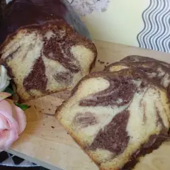 Wilgotna babka marmurkowa na oleju, oblana czekoladą, prezentuje się apetycznie obok róż.