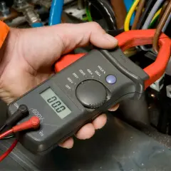 Elektryk mierzy spadek napięcia na przewodzie za pomocą cęgów mierniczych.
