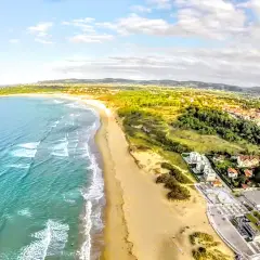 Vista aérea de la playa de Somo, con el mar turquesa, arena dorada, dunas y un pueblo costero con tejados rojos.