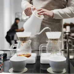 En person häller varmt vatten över kaffefilter för att brygga kaffe. En tanke på vad kostar en kopp kaffe hemma.