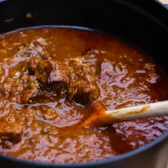 Ein dampfender Topf mit zartem Wiener Saftgulasch, das nach dem Originalrezept zubereitet wurde. Eine Holzschöpfkelle rührt in der köstlichen Sauce.