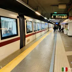 Pasażerowie czekają na peronie na metro we Włoszech. Na tablicy informacyjnej widnieje napis "Treno Successivo 4 Minuti".