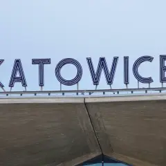 Napis "KATOWICE" z niebieskimi neonami na tle jasnego nieba.