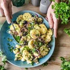 Ein köstlicher italienischer Kartoffelsalat mit Oliven, roten Zwiebeln und frischer Petersilie auf einem blauen Teller.