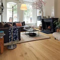 Gemütliches Wohnzimmer mit dunklem Sofa, Kamin und einem Sessel. Der used look des Holzboden und der Deko verleiht dem Raum Charakter.