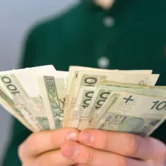 Dłonie trzymają wachlarz banknotów 100 zł. Może to być wypłata, oszczędności lub emerytura.