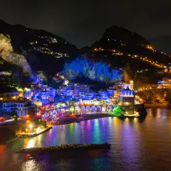 A vibrant night view of Vietri sul Mare, with buildings illuminated in colorful lights reflecting on the water.