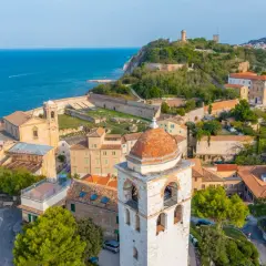 Panoramica aerea di Ancona, Marche, con il mare blu, edifici storici, un campanile e la fortezza sul colle.