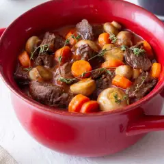Un plat rouge rempli de bœuf bourguignon facile, avec des morceaux de bœuf tendres, des carottes et des champignons, garni de thym frais.