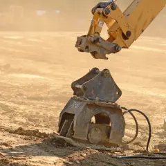 Żółty osprzęt koparki przygotowuje się do połączenia z ubijakiem. Widoczny mechanizm mocowania łyżki koparki.