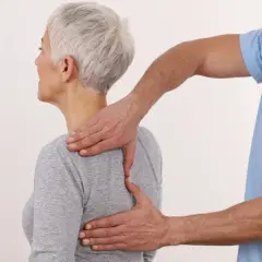 Fizjoterapeuta masuje górną część pleców i łopatki kobiety.