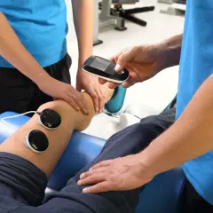 Fizjoterapeuta ustawia parametry na urządzeniu do elektroterapii, które jest stosowane na kolano pacjenta. Częstotliwość zabiegów rehabilitacyjnych zależy od stanu pacjenta.