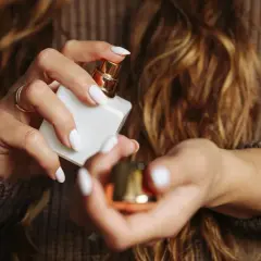 Kobieta z białymi paznokciami i złotym pierścionkiem otwiera białą buteleczkę perfum. Odkryj, jak znaleźć swój zapach perfum.