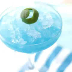 Orzeźwiający drink Błękitna Laguna, zmrożony i udekorowany skórką limonki, idealny na upalne dni.