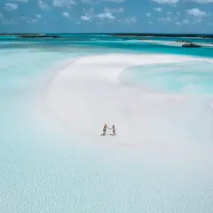Un couple se tient la main sur une plage de sable blanc aux Bahamas. L'eau turquoise et les îlots au loin invitent à explorer que faire aux Bahamas.