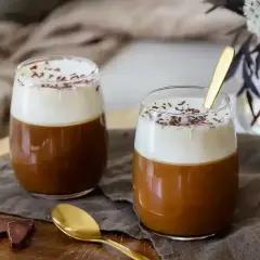 Två glas med krämig irish coffee, toppad med vispgrädde och chokladströssel. En gyllene sked vilar i det ena glaset.