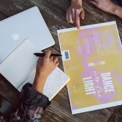 Des mains travaillent à créer une couverture de livre. Un ordinateur portable, un carnet et un brouillon de couverture sont sur une table en bois.