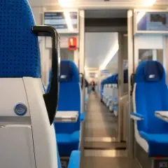 Wnętrze pociągu PKP Intercity. Siedzenia w kolorze niebieskim, rzędy foteli po obu stronach korytarza.