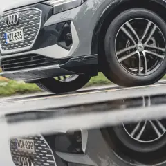 En Audi kör på en regnig väg, dess hjulbultar syns tydligt i den blöta asfalten som reflekterar bilen.