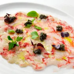 Delicado carpaccio de gambas con caviar, aceite de oliva y brotes verdes, presentado en un plato blanco.