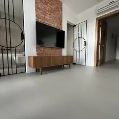 Nowoczesne wnętrze z betonową podłogą, co to jest mikrocement, która nadaje mu surowego charakteru. W tle widać łazienkę i salon.