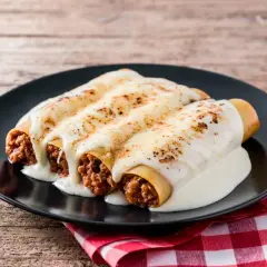 Tres canelones de carne gratinados con queso cremoso, servidos en un plato negro sobre un mantel a cuadros rojos.