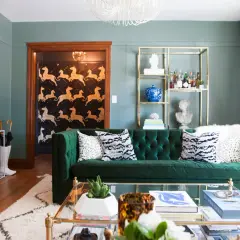 A plush emerald green sofa anchors this living room, featuring a bold zebra print wallpaper in the entryway of this 1920s craftsman house.