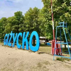 Napis GIŻYCKO na plaży, obok ratownicza wieża. Idealne miejsce na wakacje, mnóstwo giżycko atrakcje dla dzieci.
