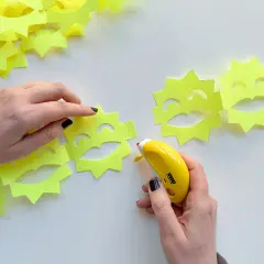Hände basteln eine ziehharmonika-girlande aus gelben Sonnen mit Gesichtern. Ein Klebestift verbindet die Elemente.