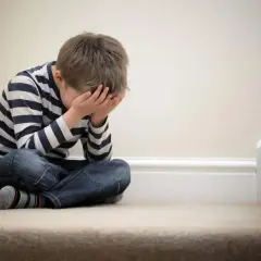 Bambino seduto sulle scale, con le mani sul viso, simbolo della delusione dei figli.